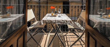 An outdoor dining area with a table set for two, a balcony with a railing, and a building in the background.
