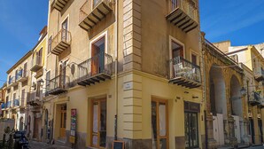 A multi-story building with balconies, a cobblestone street, and a signboard. - Angelina's apartment (Cefalù)