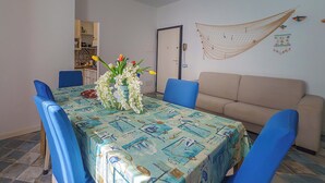A dining area with a table covered in a nautical-themed tablecloth, blue chairs, and a vase with white flowers. - Angelina's apartment (Cefalù)