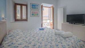 A bedroom with a bed, a television, a balcony, and two framed pictures on the wall. - Angelina's apartment (Cefalù)