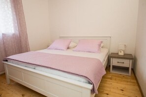 A neatly made bed with a pink blanket and pillows, a bedside table with a lamp, and a wooden floor. - Villa in a Sunny Trbounje Zone (Drnis)