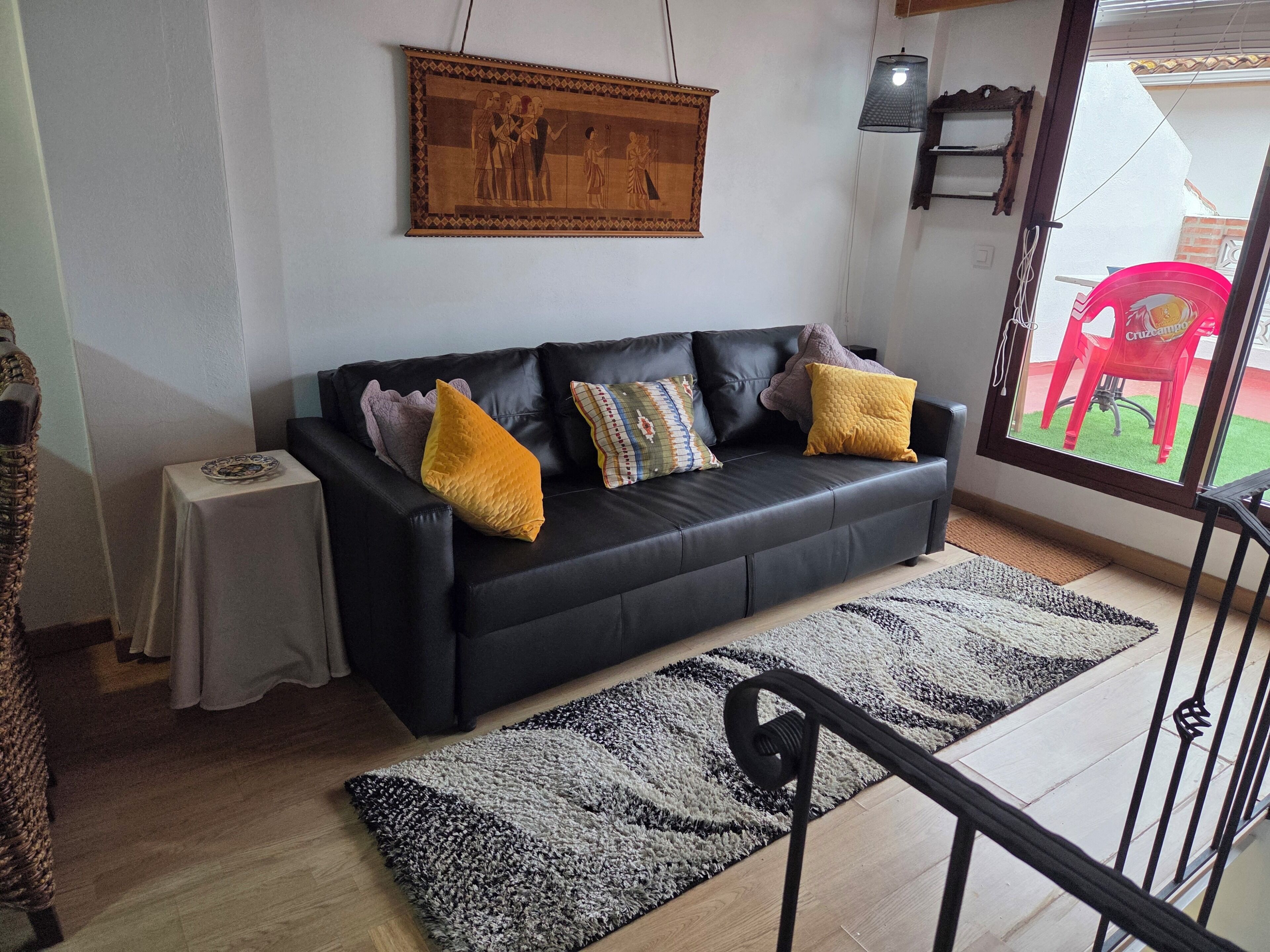 A living room with a black leather sofa, a small white table, a patterned rug, and a framed picture on the wall.