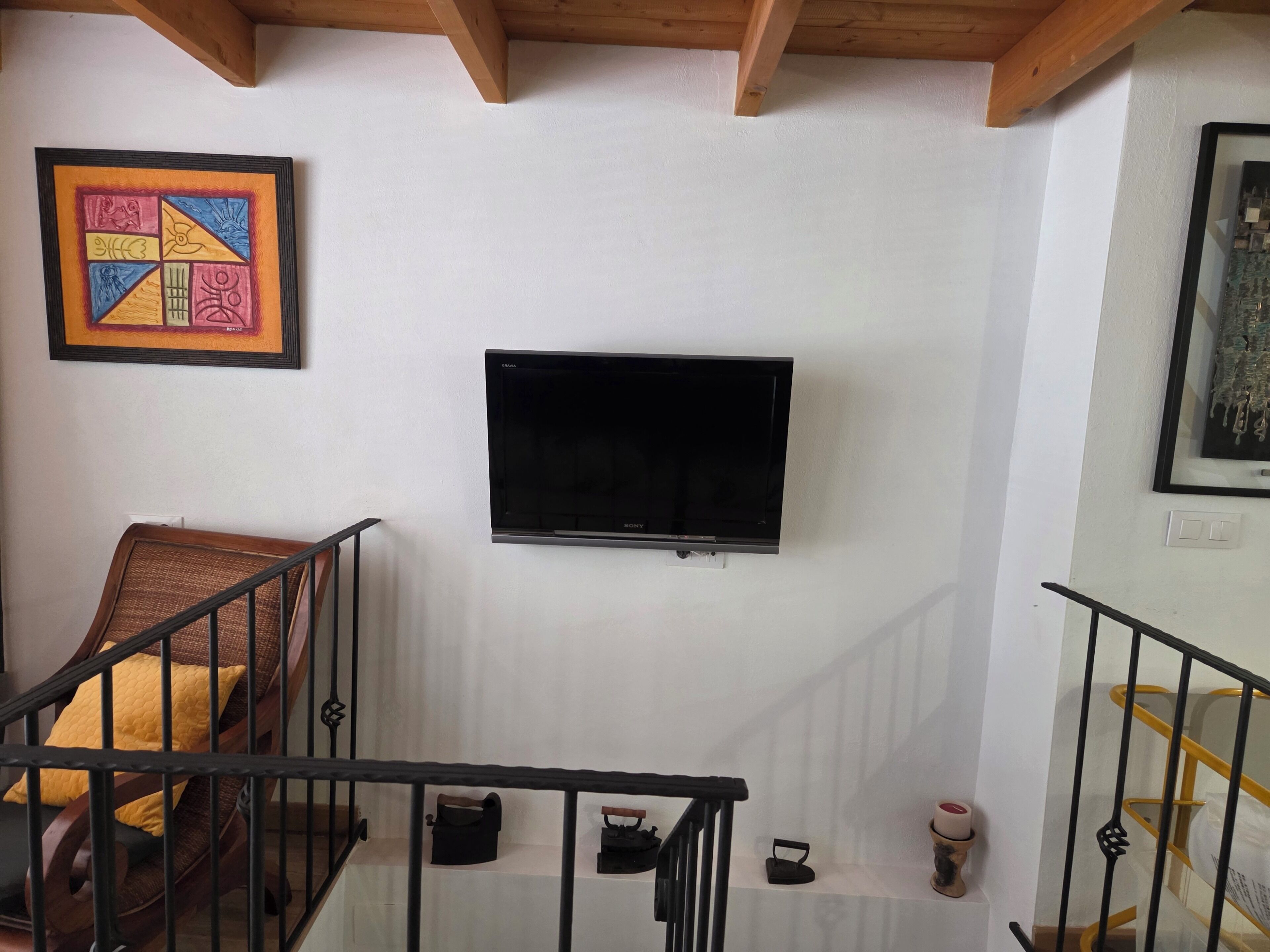 Un escalier avec une rampe noire, un téléviseur à écran plat noir fixé au mur et une œuvre d’art encadrée au-dessus du téléviseur.