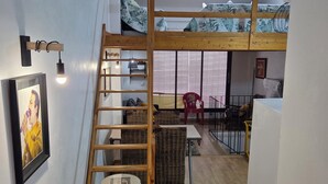 Ein Loft-Zimmer mit Holzleiter, Etagenbett, kleinem Tisch und Stuhl.
