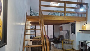 Ein Loft-Zimmer mit einer Holzleiter, die zu einem Stockbett führt, einem kleinen Tisch und einer Waschmaschine.