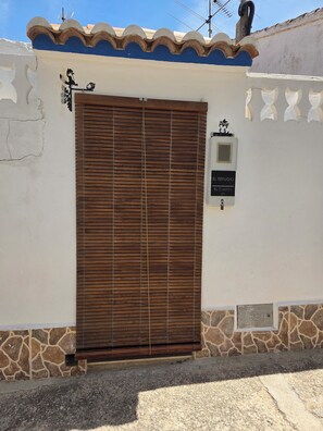 A closed wooden door with a sign reading 'EL REFUGIO EL CASTILLO' on a white wall with stone accents.