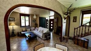 Un salón espacioso con sofá, una mesa de centro y una chimenea. Se observa una escalera con barandilla de madera y un ciervo montado en la pared.