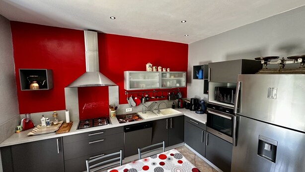 Una cocina moderna con electrodomésticos de acero inoxidable, una pared de acento roja y un microondas integrado.