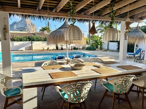 Un espace aménagé au bord de la piscine, avec une table dressée pour les repas, entourée de chaises, et une piscine avec des chaises longues.