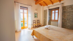 Un dormitorio con cama, sillas de madera, pared de piedra y ventana.