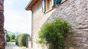 Edificio de piedra con camino de grava, vigas de madera y contraventanas verdes.