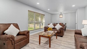 A modern living room with two brown leather sofas, a wooden coffee table with a vase of sunflowers, and a dining area in the background. - Home in Dallas / Entire Home (Dallas)