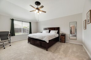 A bedroom with a bed, a ceiling fan, a window with curtains, a chair, a dresser, and a mirror. - 4BR Dream Home Close to Lake Beach, PGA, Universal Kids. Private outdoor deck. (Little Elm)