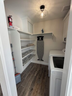 A laundry room with a washing machine, a drying rack, a broom, and a fire extinguisher. - 4BR Dream Home Close to Lake Beach, PGA, Universal Kids. Private outdoor deck. (Little Elm)