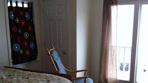 Un dormitorio con una cama, un sillón mecedora, una puerta y una ventana con cortinas.