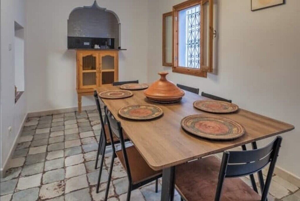 A dining area with a wooden table set for four, a rustic oven, and a window with bars.