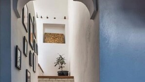 A hallway with a brick staircase, framed artwork on the walls, and a potted plant on the landing. - EL SAMA' PRIVATE ROOFTOP HOUSE 80M2 HEART OF OLD MEDINA (Chefchaouen)