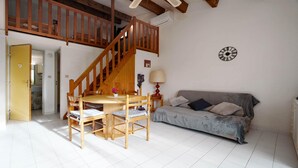 Een gezellige kamer met een houten trap, een eettafel met stoelen, een bank en een wandklok.