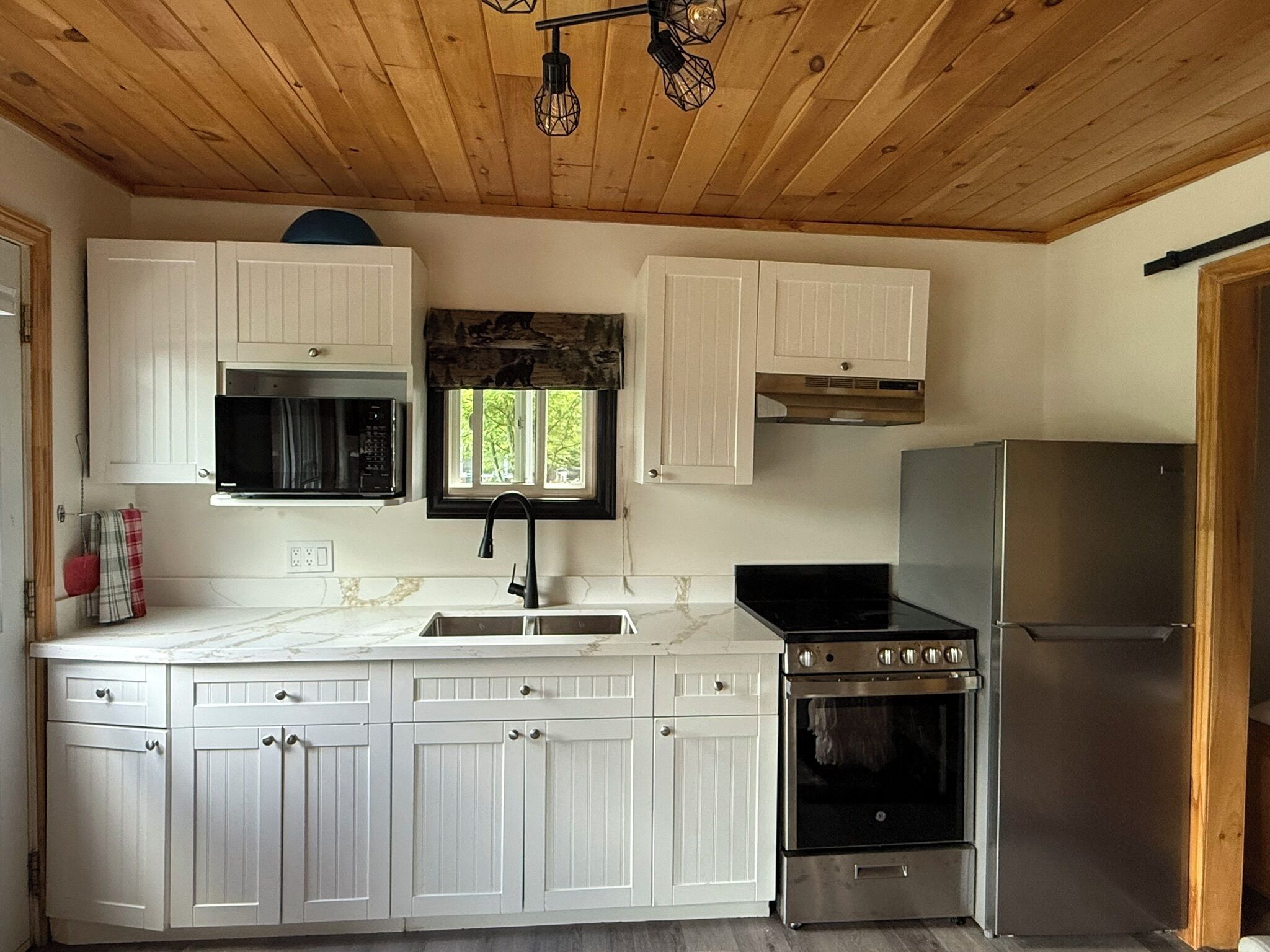 Una cocina con armarios blancos, un refrigerador de acero inoxidable, estufa y microondas.