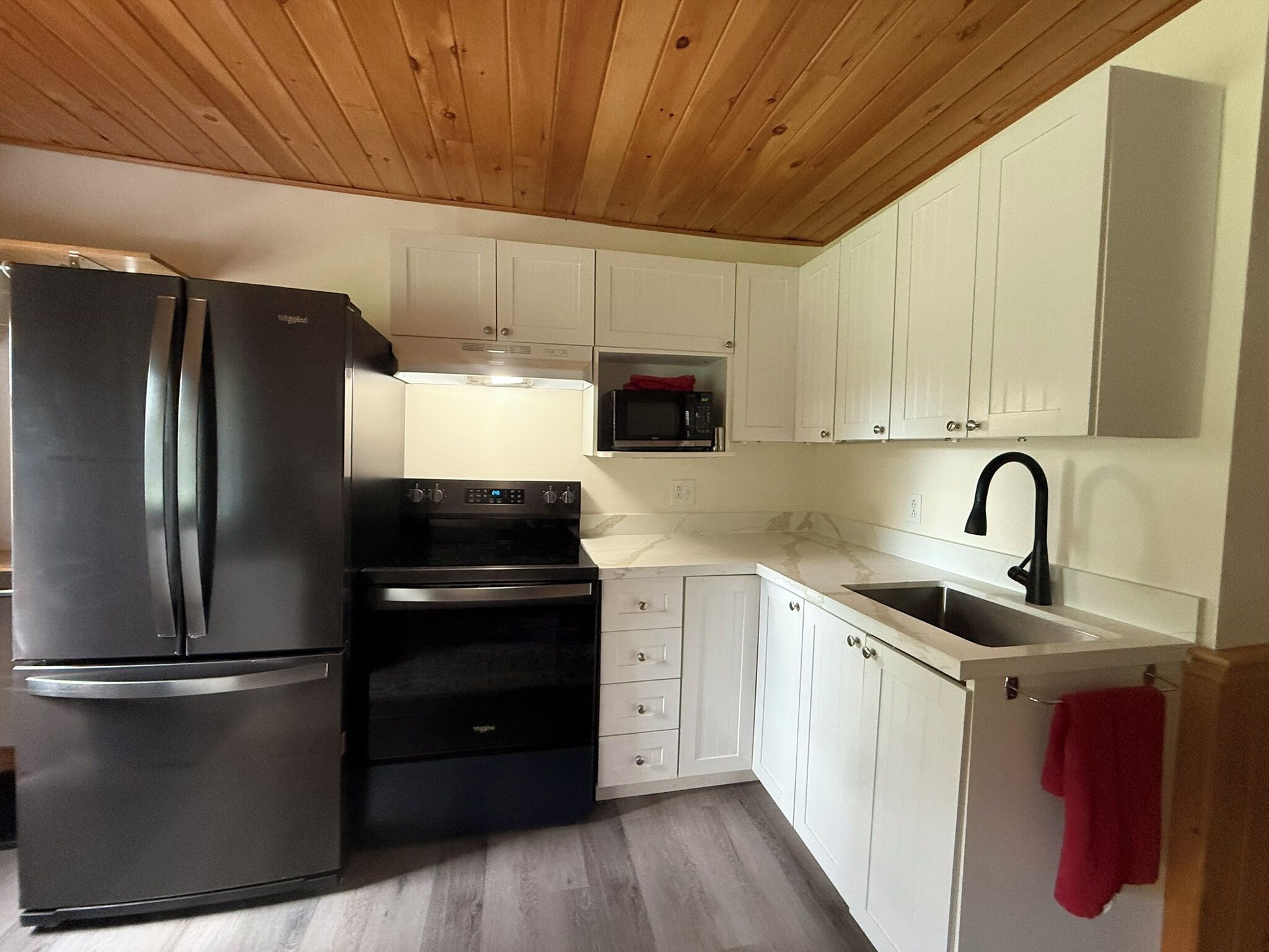 A compact kitchen with white cabinets, a black refrigerator, a stove, and a microwave.