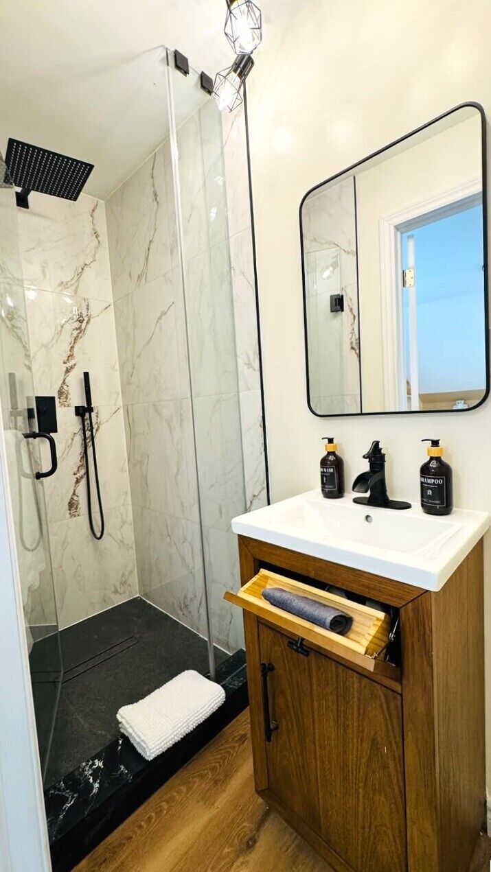 Un baño con ducha, lavabo con espejo y armario de madera.