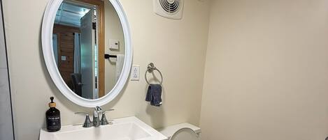 A bathroom with a white vanity, a round mirror, a toilet, and a hand soap dispenser.