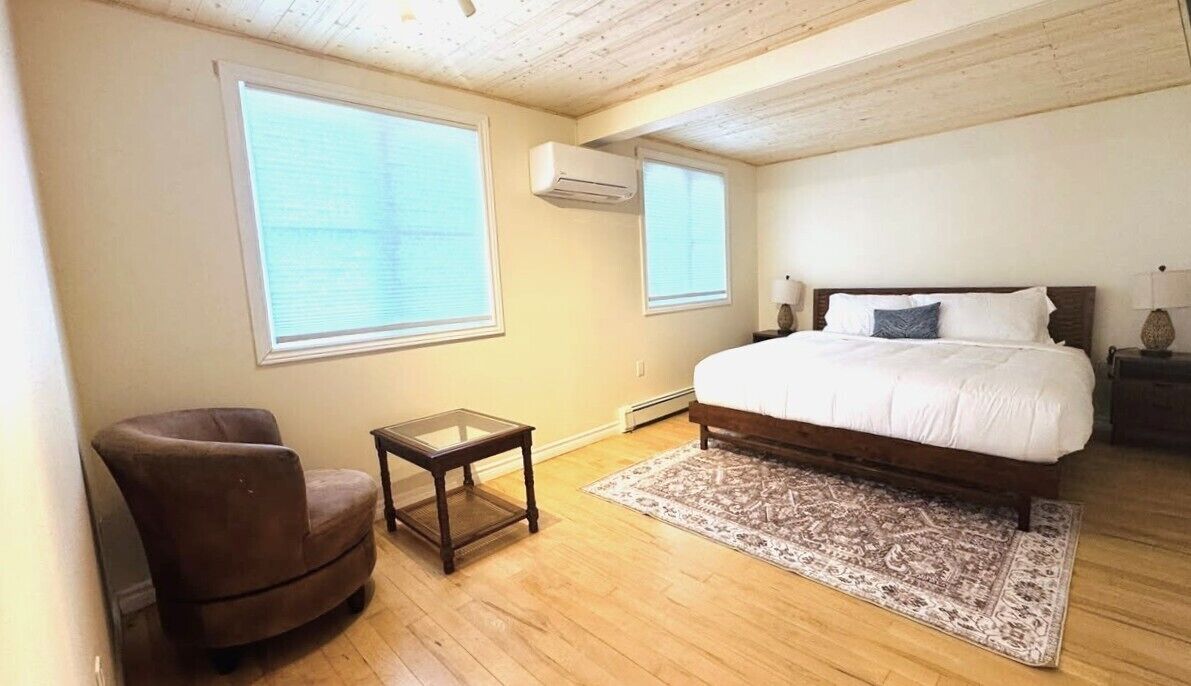 A bedroom with a bed, a chair, a small table, and a rug.