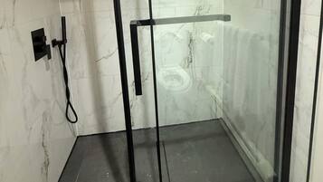 Cabina de ducha con paredes de vidrio y marco negro, un cabezal de ducha manual y un perchero para toallas.
