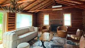 A log cabin interior with a sofa, chairs, a fireplace, and a ceiling fan.