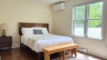 A bedroom with a bed, a bedside table, a lamp, a bench, and a window with a view of trees.