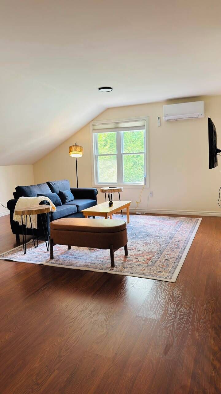 Un espacio tipo loft con un sofá azul oscuro, una mesa de centro de madera, un tapete estampado y un ventanal grande.
