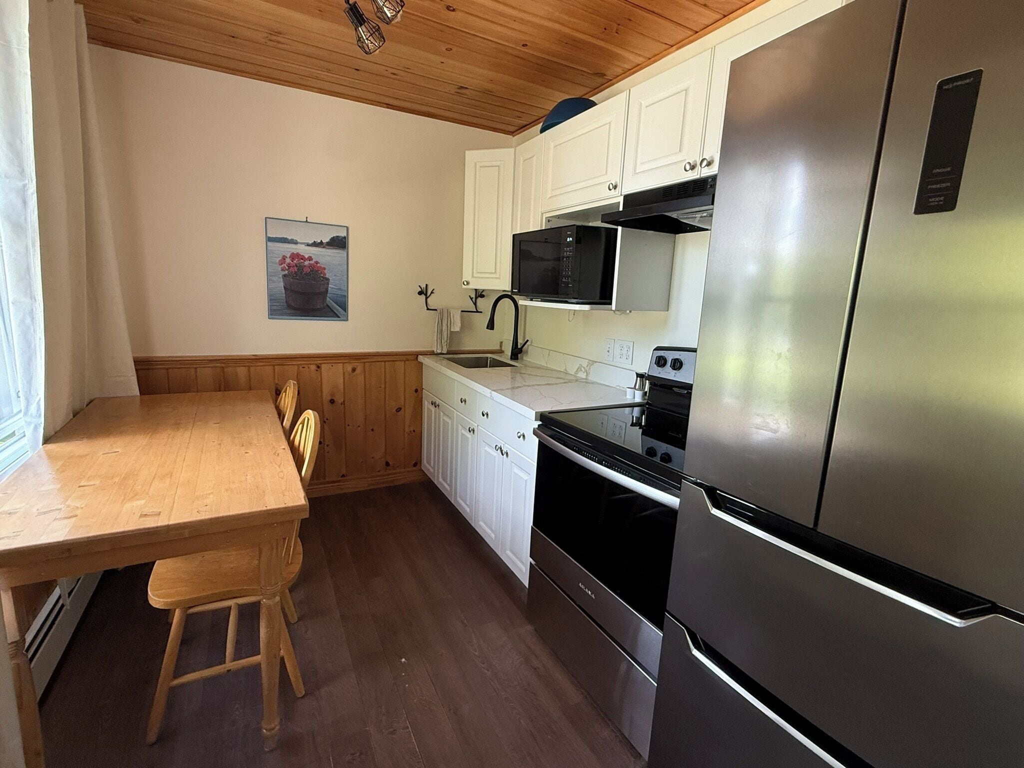 A compact kitchen with white cabinets, a stainless steel refrigerator, a microwave, and an oven.