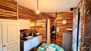 A compact kitchen with wooden walls, a sink, and a dining area with a table set for two. - Cabin-style Nook for 2 (Mont-Dore)