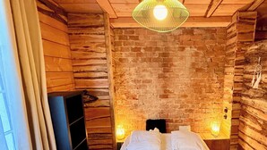 A cozy room with a brick wall, wooden ceiling, and a bed with white linens. - Cabin-style Nook for 2 (Mont-Dore)