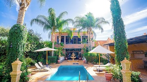 Un espace piscine aménagé avec des chaises longues, des parasols et une fontaine.