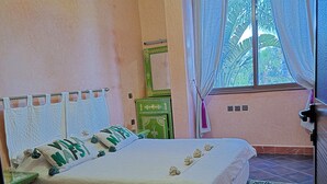 A bedroom with a bed, a nightstand, a mirror, and a window with curtains.