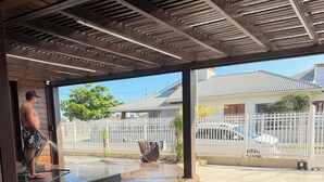 Un espace extérieur abrité, doté d’un sol carrelé, d’un tuyau d’arrosage et d’une personne se tenant près d’une porte.