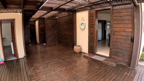 Une terrasse en bois couverte, au design rustique, dotée d’une porte et d’un luminaire fixé au mur.