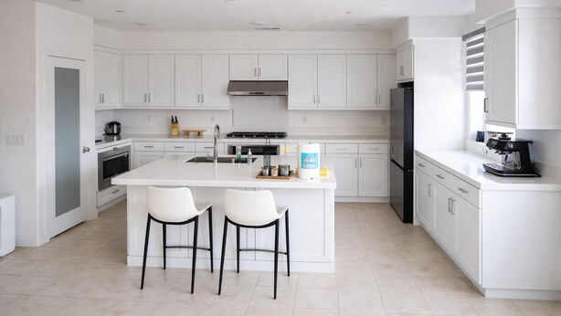 Een moderne keuken met witte kasten, een centraal eiland met twee barkrukken, een inbouwoven en een koffieapparaat.