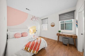 A bedroom with a bed, bedside table, lamp, and a window with blinds.