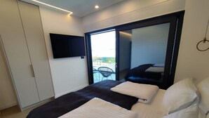 A modern hotel room with a large bed, a flat-screen TV mounted on the wall, and a sliding glass door leading to a balcony with outdoor furniture. - Serene Rovanjska Villa for 10 (Jasenice)