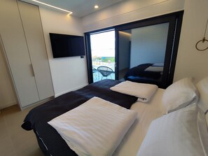 A modern hotel room with a large bed, a flat-screen TV mounted on the wall, and a sliding glass door leading to a balcony with outdoor furniture. - Serene Rovanjska Villa for 10 (Jasenice)