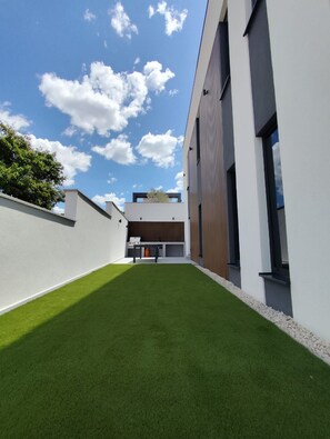 Un bâtiment moderne doté d’un toit plat, de grandes fenêtres et d’une terrasse sur le toit, également plate, recouverte de gazon synthétique.