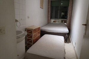 A small, narrow room with a bed, a wooden chest of drawers, and a window with curtains. - PROMENADE DES ANGLAIS, 1 BEDROOM, AIR CONDITIONING, GARAGE (Nice)