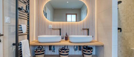 A modern bathroom with two sinks, a large mirror, and a shower.