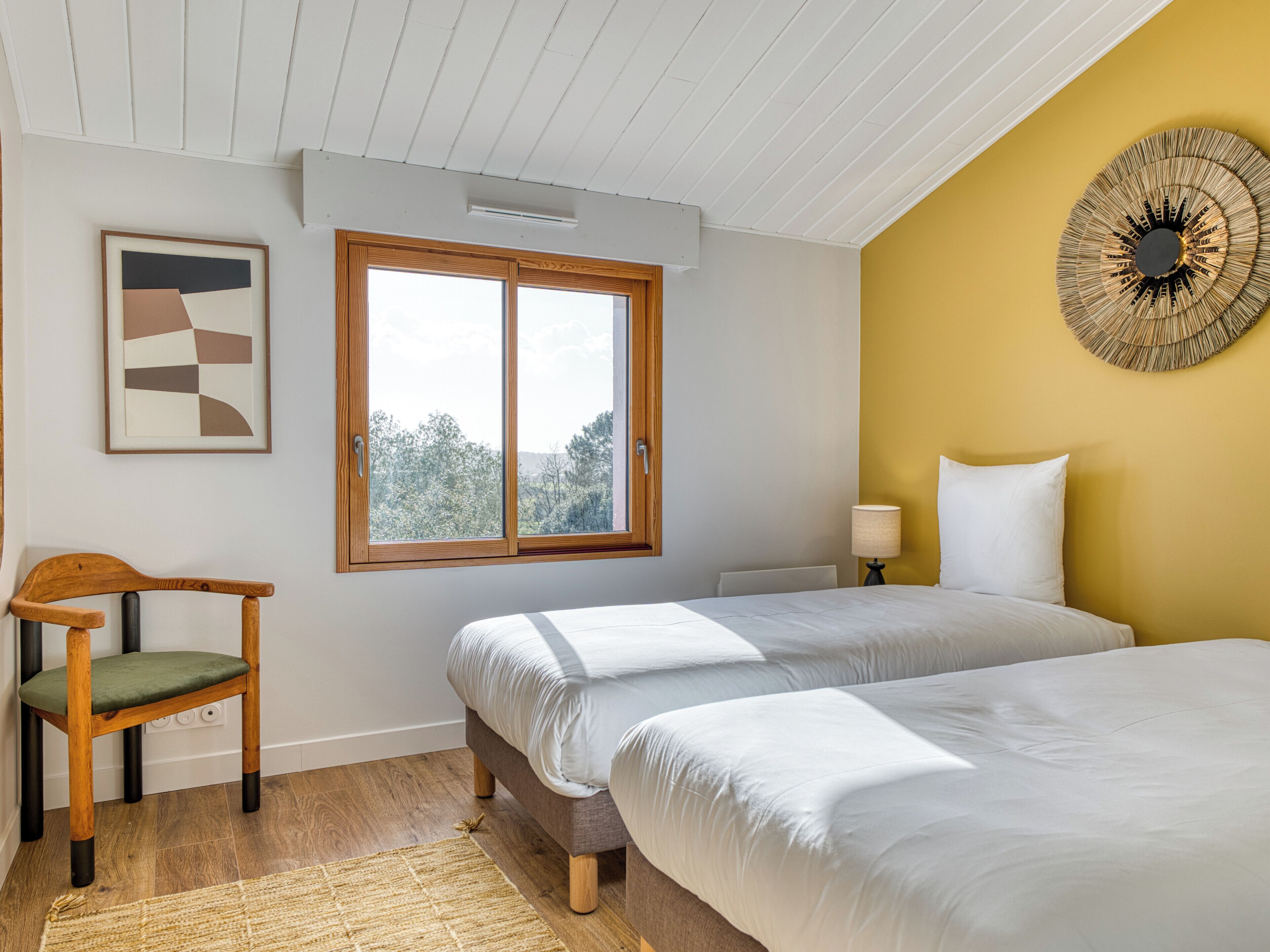 A bedroom with two beds, a window, a chair, a lamp, and a wall decoration.