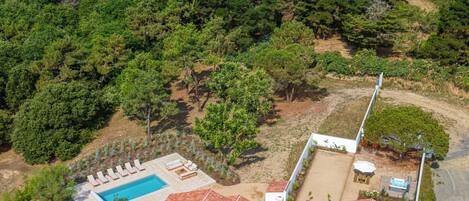 An aerial view of a property with a swimming pool, multiple buildings, and surrounding greenery.