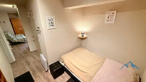 A small, cozy bedroom with a single bed, a bedside table with a lamp, and two framed pictures on the wall. - Quiet Corner Near the Mountain Road (Mont-Dore)