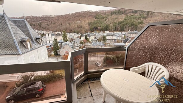A balcony with a view of a town, a chair, and a car. - Quiet Corner Near the Mountain Road (Mont-Dore)