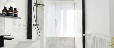 Un baño moderno con ducha envuelta en vidrio, una bañera blanca y un salpicadero de mármol.